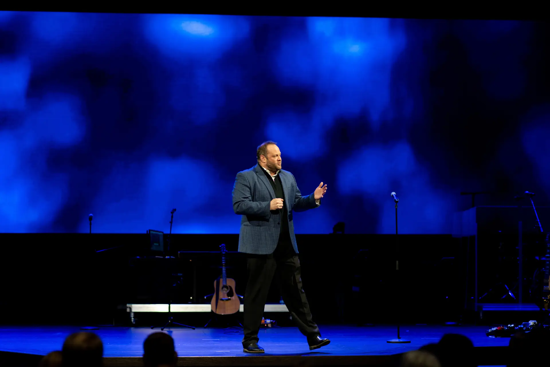 Cameron Mills speaking on a stage lit in blue