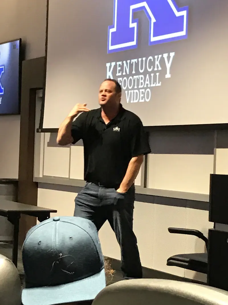 Cameron Mills speaking to a group in a University of Kentucky football meeting room